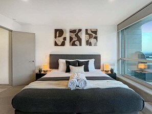 A modern hotel room with a large bed, a view through a glass wall, and abstract wall art. - Charming Retreat | Balcony, Views and Garage (Queenstown)