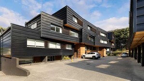 Un edificio moderno de varios pisos con techo plano, ventanas amplias y un estacionamiento con coches.
