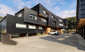 A modern multi-story building with a flat roof, large windows, and a parking area with cars. - Hallenstein Street Retreat, 3Bedroom Queenstown Home (Queenstown)