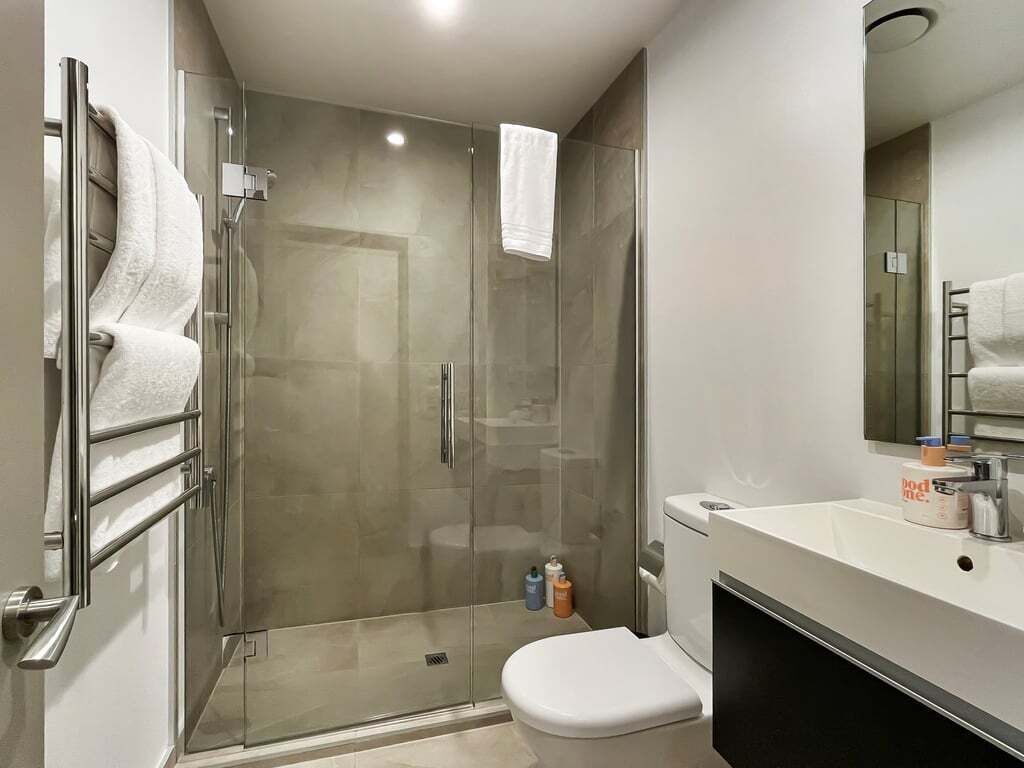 Une salle de bain moderne avec une douche à parois de verre, des toilettes blanches et un meuble-lavabo avec un miroir.