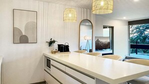 Una cocina moderna con una isla central, iluminación colgante y un ventanal grande.