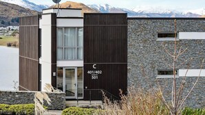 A modern building with a stone facade and a wooden section, featuring a large window and a satellite dish. - Sunlit Serenity, Lakefront Apartment (Kawarau Falls)