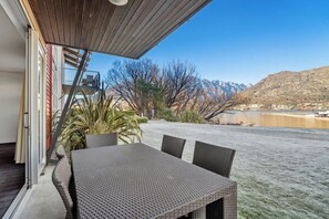 Un patio con una mesa y sillas, una planta en maceta y vistas a montañas y un lago.