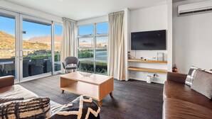 A modern living room with a large window, a flat-screen TV, a sofa, a coffee table, and a chair. - Waterfront 3 Bedroom Marina Gem (Queenstown)