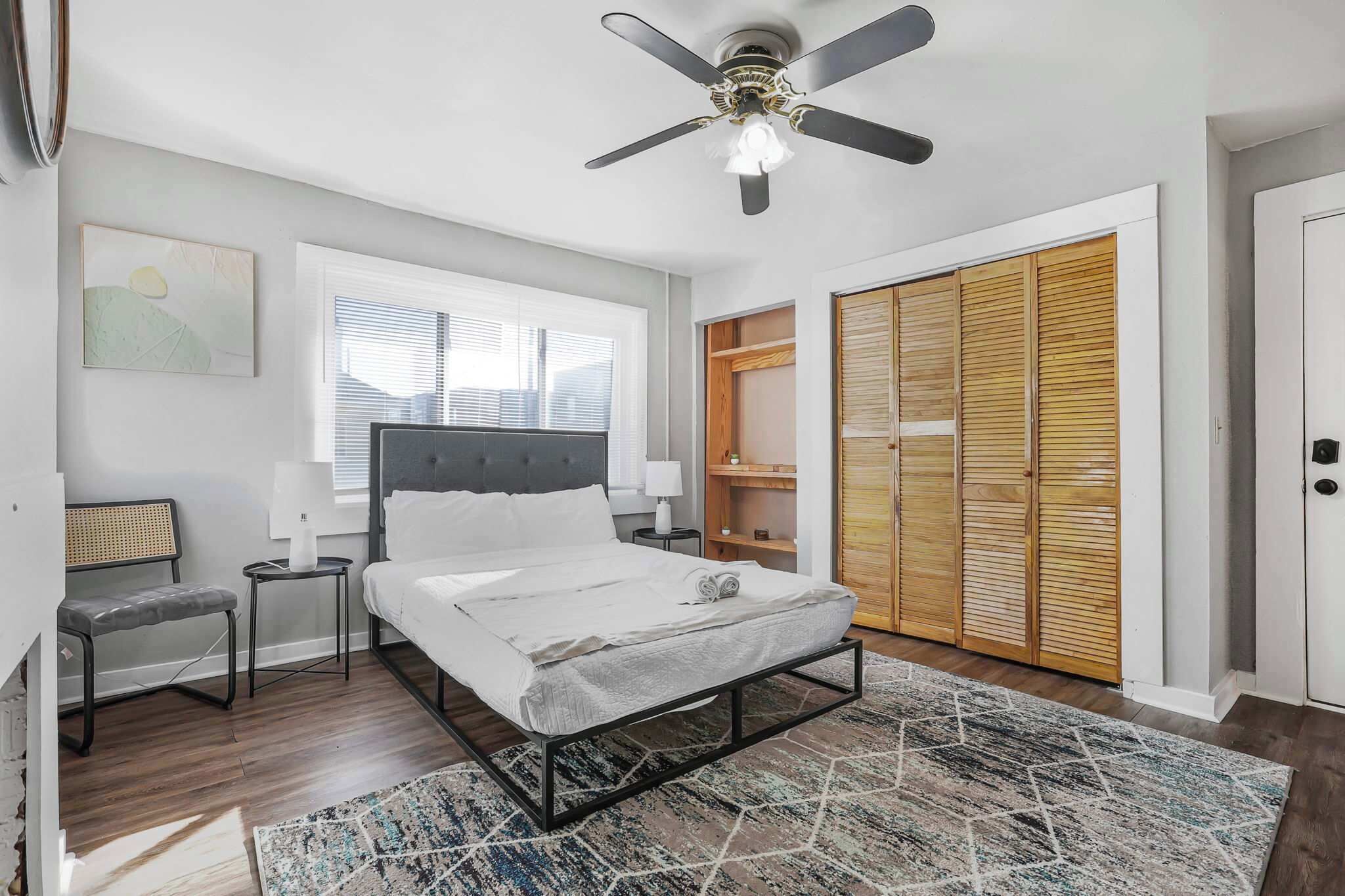 Une chambre à coucher comprenant un lit, des tables de chevet, un ventilateur de plafond, une fenêtre et une armoire.