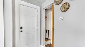 Un couloir avec une porte blanche, un banc en bois et un thermostat fixé au mur.