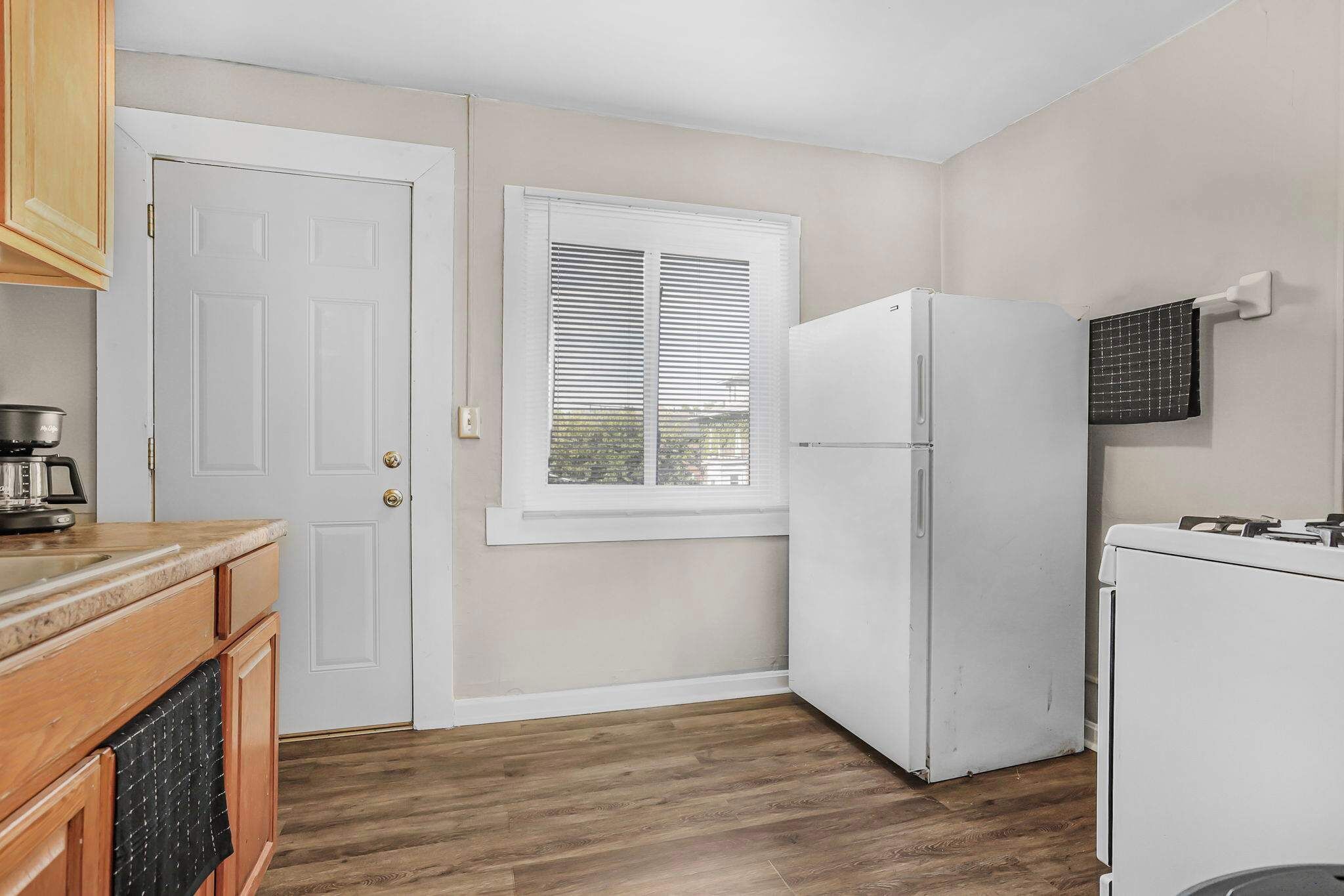 A kitchen with wooden cabinets, a white refrigerator, and a window with blinds.