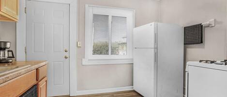 A kitchen with wooden cabinets, a white refrigerator, and a window with blinds.