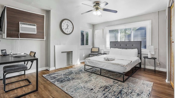 Une chambre à coucher comprenant un lit, des tables de chevet, un bureau, une chaise, un ventilateur de plafond, une horloge et une fenêtre.