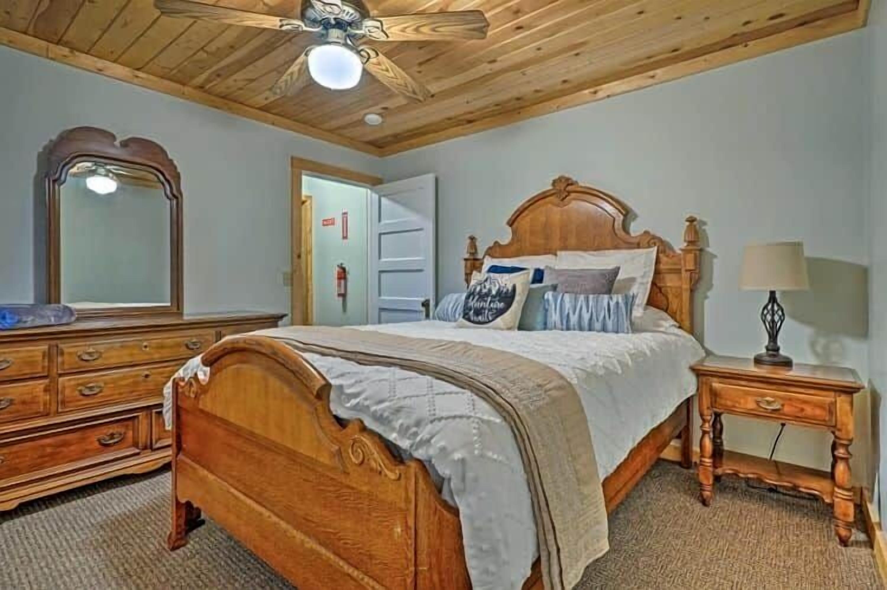 A bedroom with a wooden bed, a nightstand, a dresser, and a ceiling fan.