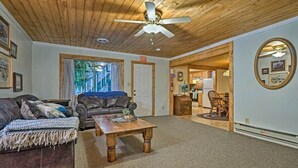 A cozy living room with a wooden ceiling, a ceiling fan, a fireplace, and a dining area with a table and chairs. - The Residence on Main (Pioche)