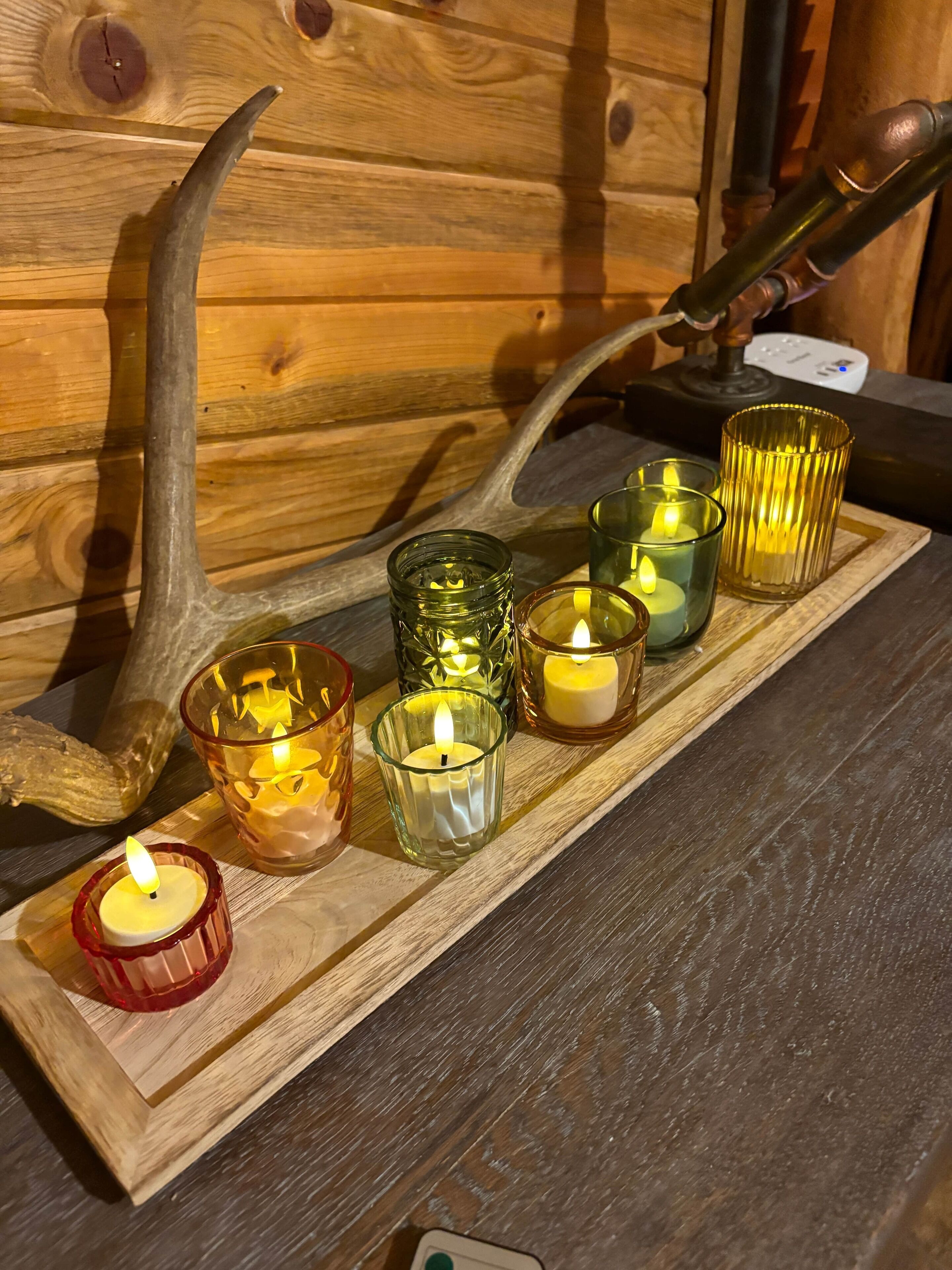 A wooden tray with candles in various glass holders.