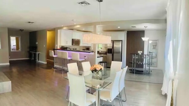 A modern dining area with a glass table and white chairs, a kitchen in the background, and a large window with curtains. - "Monthly Stay • Pool - WiFi - Parking - Near Strip (Las Vegas)