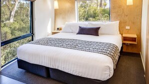 Une chambre moderne avec un grand lit, une vue sur les arbres par la fenêtre et un panneau mural en bois.