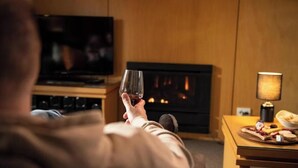 Une personne tenant un verre dans une pièce où se trouvent une cheminée, un téléviseur et une table avec de la nourriture.