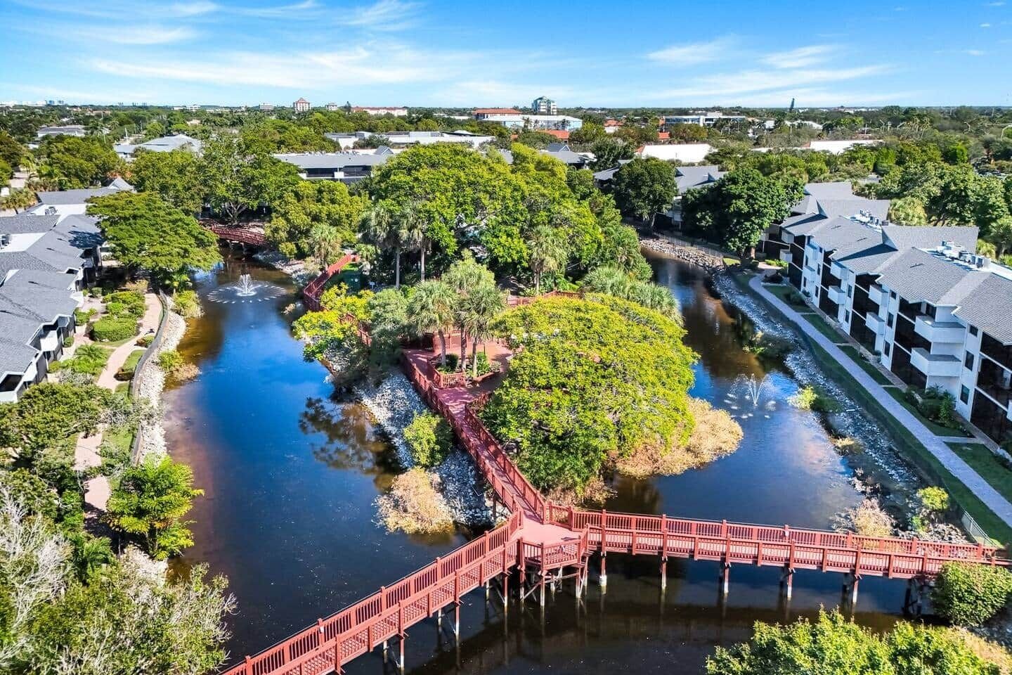 A riverside view with a red bridge, modern buildings, and lush greenery.