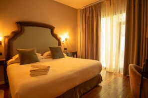 A hotel room with a large bed, two pillows, a bedside table, a lamp, and a chair. - Hotelate (Úbeda)