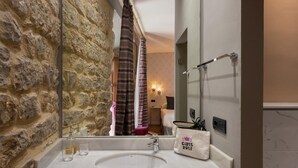 Une salle de bain avec un mur en pierre, un lavabo blanc, un miroir et un porte-serviettes.