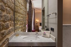 A bathroom with a stone wall, a white sink, a mirror, and a towel rack. - Hotelate (Úbeda)