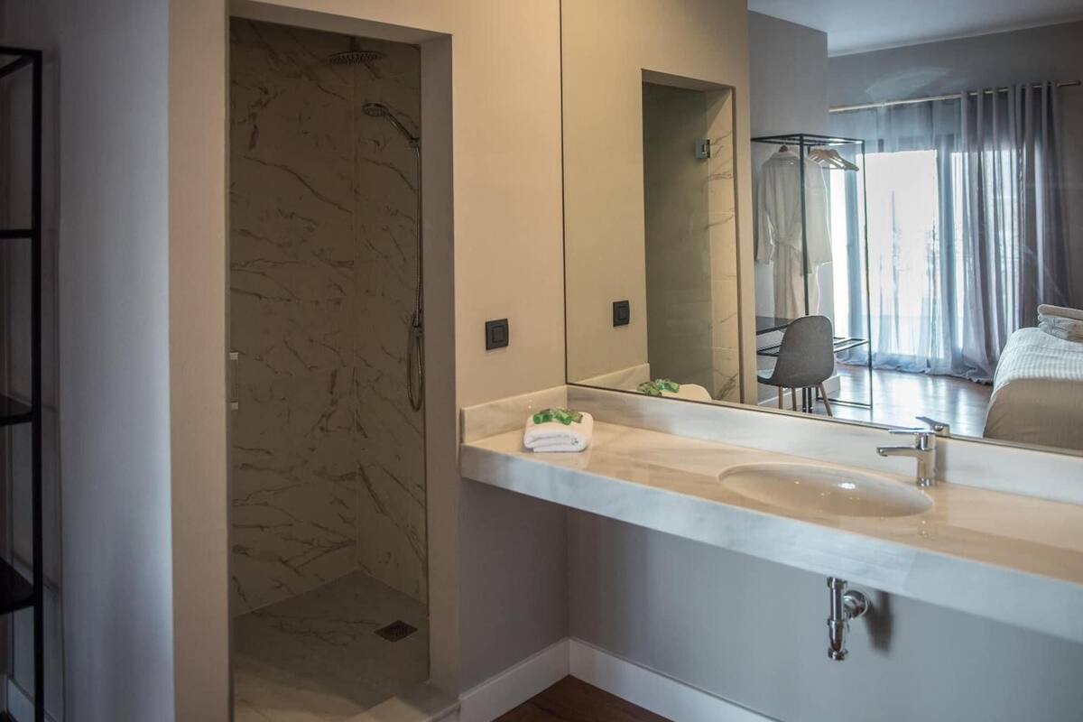 Un baño moderno con cabina de ducha de mármol, un espejo grande y un lavabo.