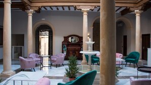 A spacious lobby with marble flooring, multiple seating areas including plush armchairs and a round table, and a central fountain. - Hotelate (Úbeda)