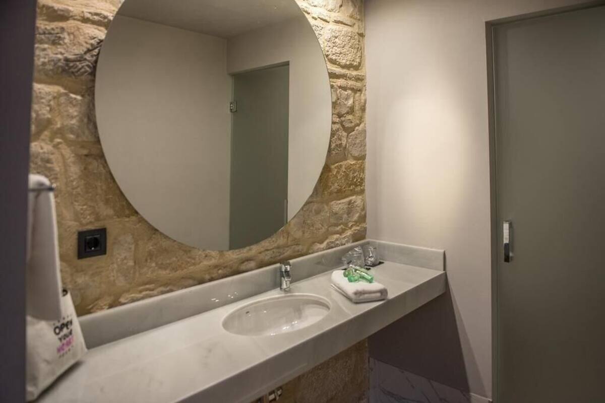 Un baño con pared de piedra, un espejo redondo, un lavabo y una puerta.