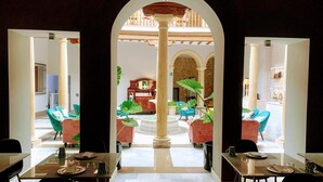 A dining area with tables and chairs, a central column, and a view of a room with a bed and a dresser. - Hotelate (Úbeda)