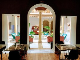 Un comedor con mesas y sillas, una columna central y vista a una habitación con cama y cómoda.