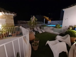 Una terraza en la azotea con piscina, sillones de descanso y plantas en macetas.