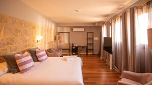 A hotel room with a large bed, a desk, a chair, a TV, and a stone wall. - Hotelate (Úbeda)