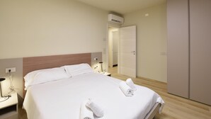 A hotel room with a neatly made bed, a bedside lamp, an air conditioning unit, and a wardrobe.