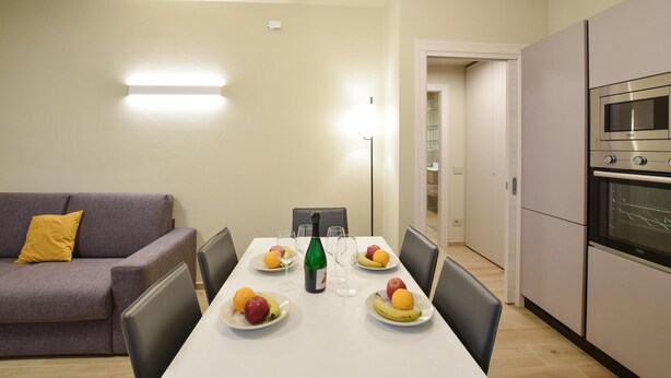 A modern kitchen with a dining table set for four, a sofa with a yellow pillow, and a large oven.