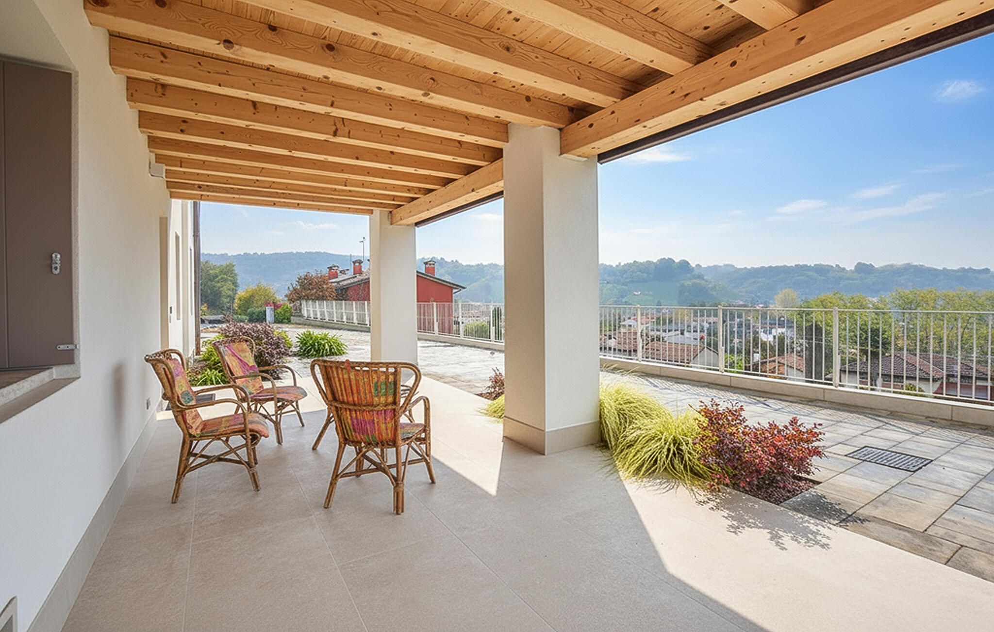 A covered outdoor area with a table and chairs, a view of the landscape, and a building in the background.