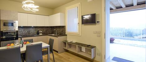 A modern kitchen with a dining area, built-in oven, and a TV mounted on the wall.