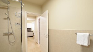A bathroom with a shower, a towel rack, and a door leading to a kitchen area.