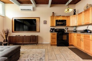 Una cucina moderna con mobili impiallacciati in legno, un piano cottura nero, un forno a microonde e un ampio televisore a schermo piatto montato a parete.