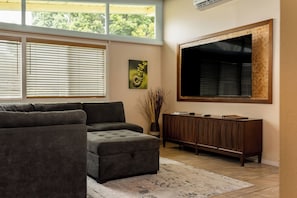 A living room with a sectional sofa, a flat-screen TV mounted on the wall, and a cabinet. - Hale Hibiscus (Hilo)