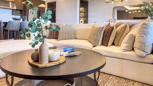 Ein modernes Wohnzimmer mit einem Ecksofa, einem runden Couchtisch und einem Essbereich im Hintergrund.
