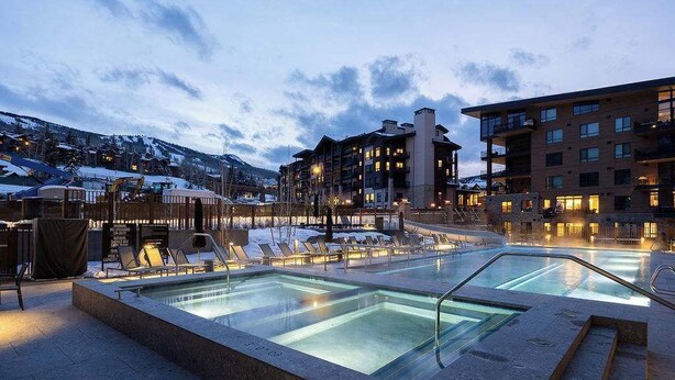 Ein Hotelpoolbereich mit mehreren Liegestühlen und einem klaren Pool, umgeben von Gebäuden mit Balkonen und Beleuchtung.