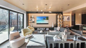 Ein modernes Wohnzimmer mit großem Fernseher, bequemen Sitzgelegenheiten und Blick ins Freie.