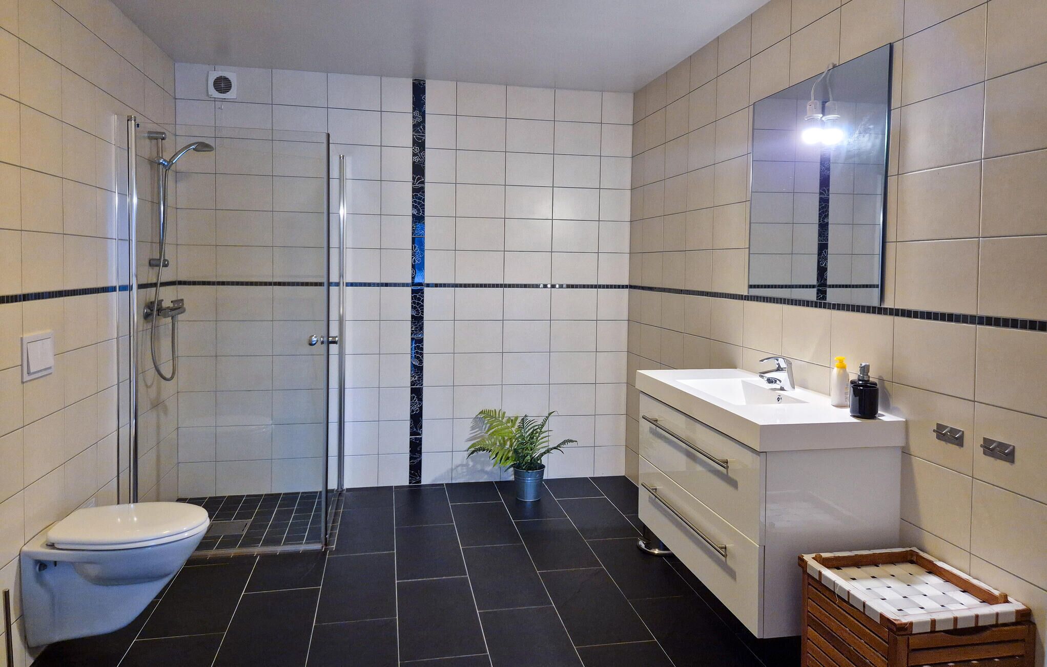 A bathroom with a toilet, shower, sink, and a potted plant.