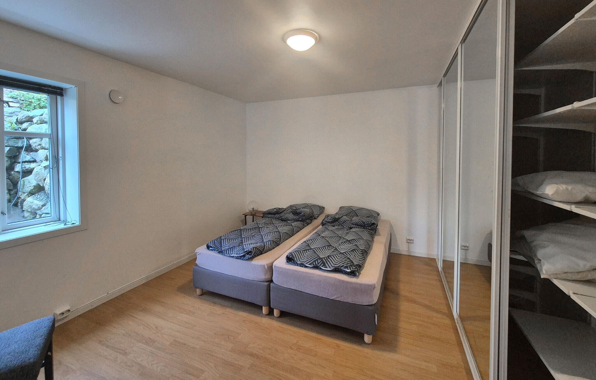 Quarto pequeno com duas camas de solteiro, uma janela e um guarda-roupa com prateleiras.