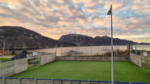 A sports field with a goalpost and a flagpole, surrounded by a fence and a mountainous backdrop.