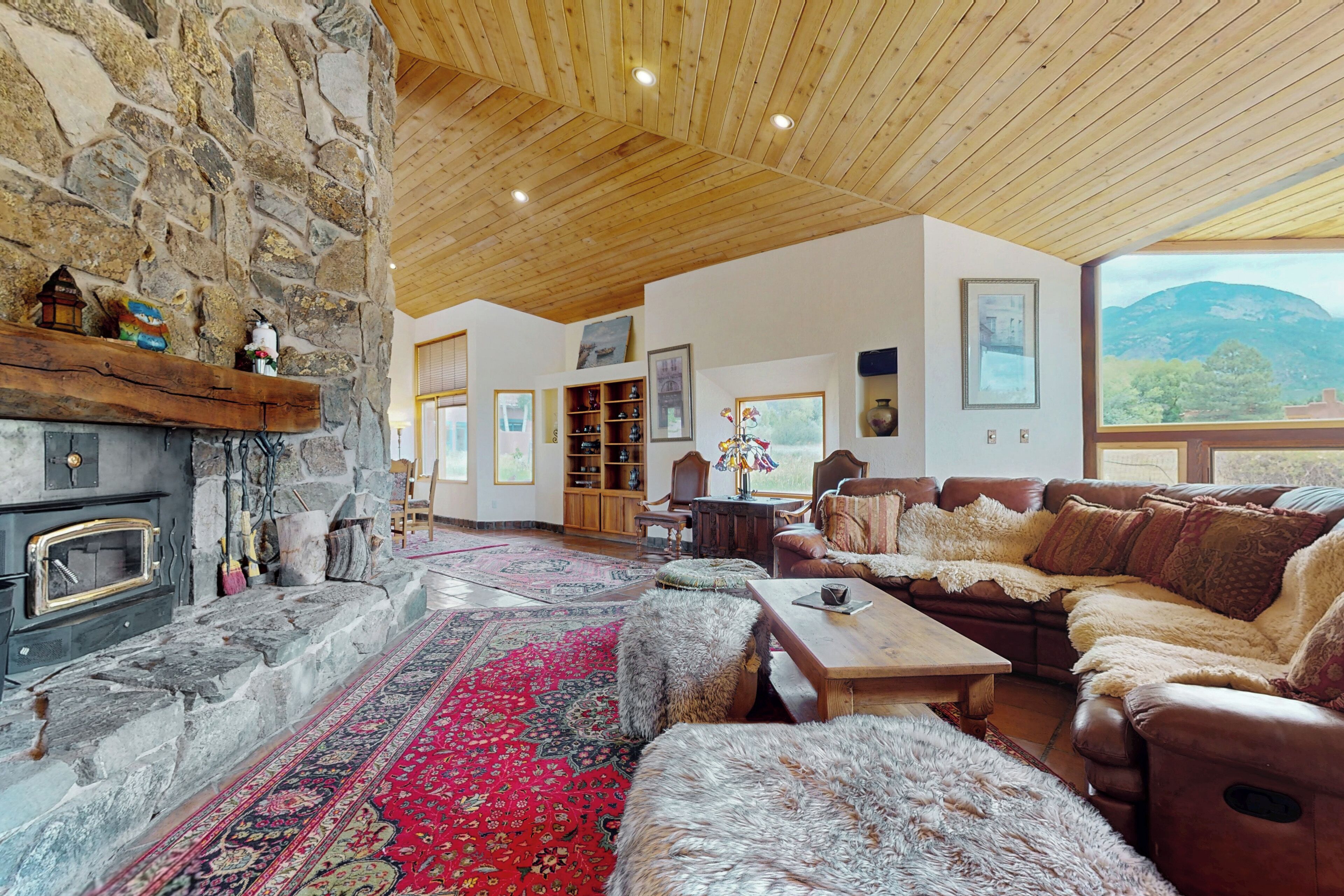 A cozy living room with a stone fireplace, wooden ceiling, and a large window offering a mountain view.