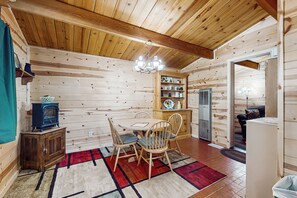 A wooden cabin interior with a dining table, chairs, a chandelier, a small cabinet, and a refrigerator. - 7 Mi to Ski Resorts: Dog-Friendly Sugarloaf Cabin (Sugarloaf)