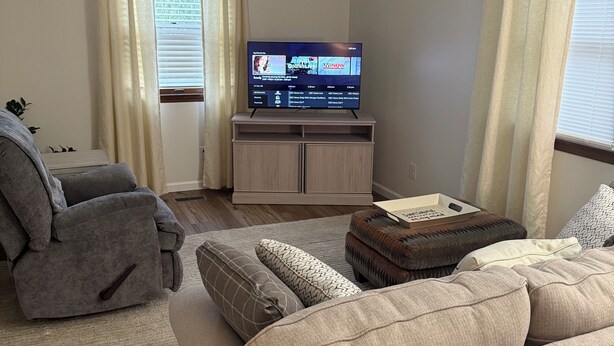 A living room with a beige sofa, a grey recliner, a flat-screen TV on a wooden stand, and a window with curtains. - Comfortable Modern Stay Quiet 1BR Retreat Near Dayton, Eaton, Miami U& Richmond (Eaton)