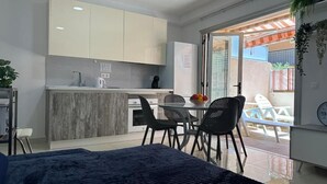 Cozinha moderna com armários brancos, área de jantar com mesa e cadeiras, e uma porta de vidro deslizante para um pátio externo.