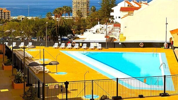 Piscina no terraço com espreguiçadeiras, vista para o mar e edifícios ao fundo.