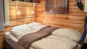 Une pièce aménagée comme un chalet en bois, avec un lit, deux lampes fixées au mur et un tableau accroché au mur.