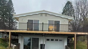 A two-story house with a garage, a covered front porch, and a fenced backyard. - Lake View 2BR - 2-Min Walk to Sandy Beach - Sleeps 4-6 - Boyne City (Boyne City)